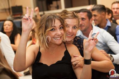 Des personnes dansent en ligne dans une salle décorée de ballons, avec des tables dressées et des convives en arrière-plan.