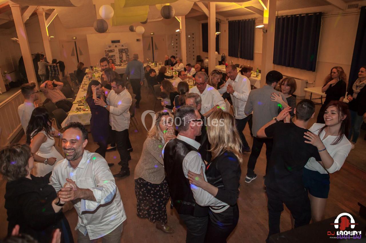 Des personnes dansent et discutent dans une salle de réception éclairée, décorée pour un événement festif.
