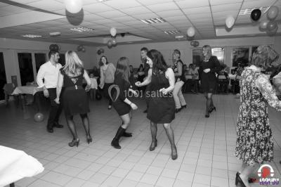 Des personnes dansent en ligne dans une salle décorée de ballons, avec des tables dressées et des convives en arrière-plan.