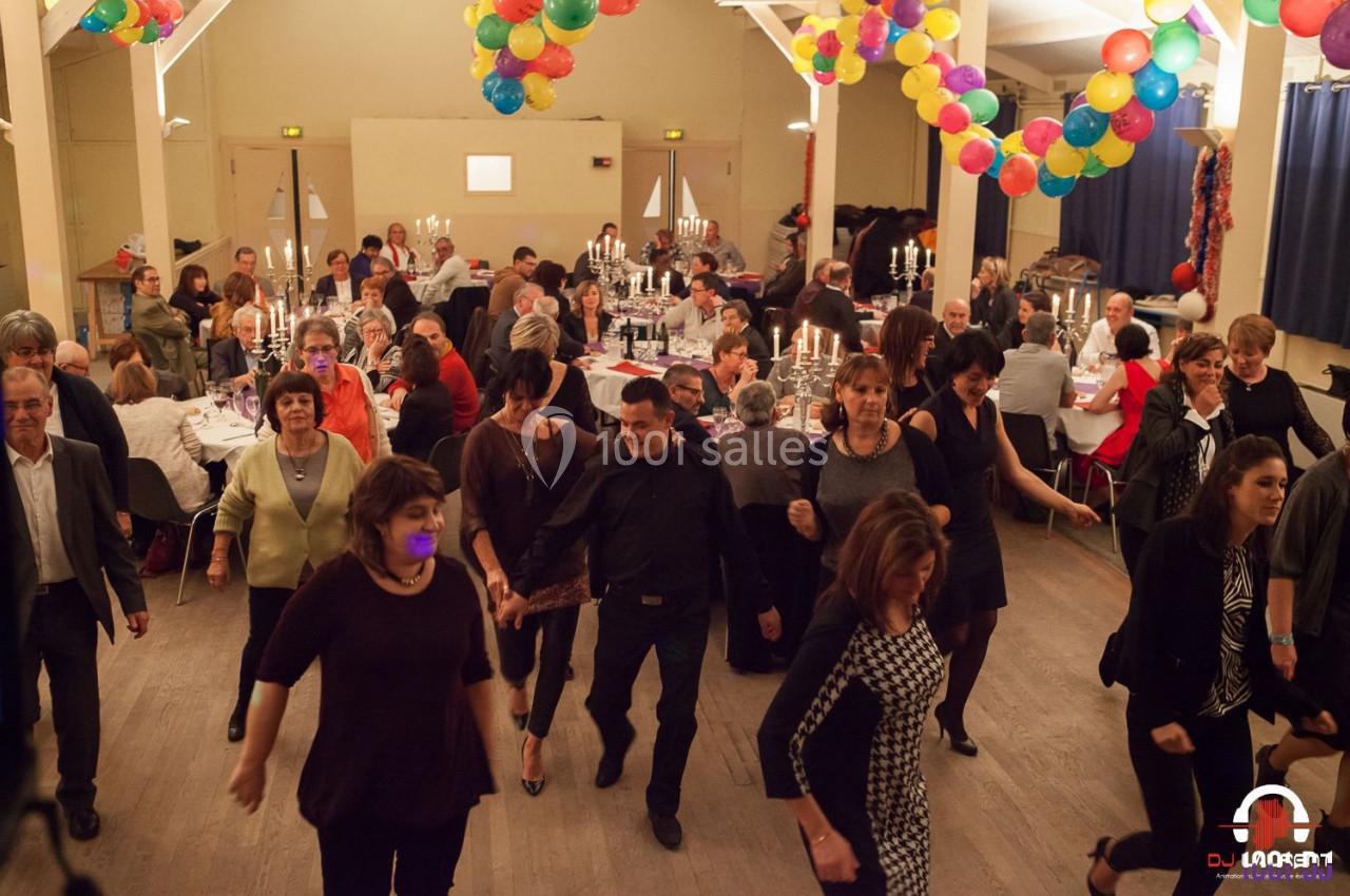 Des personnes dansent en ligne dans une salle décorée de ballons, avec des tables dressées et des convives en arrière-plan.