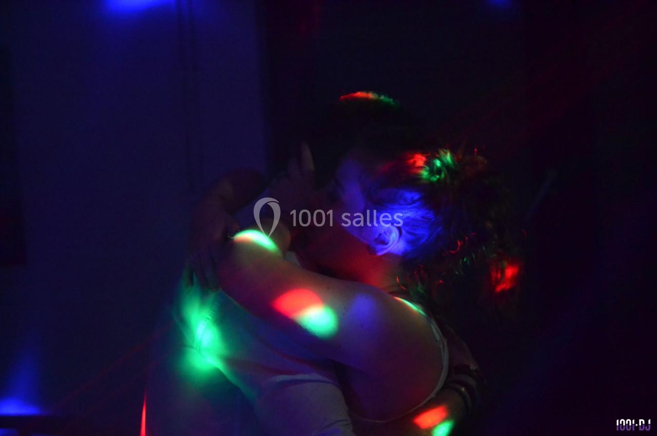 Deux personnes s'enlacent dans une ambiance sombre éclairée par des lumières colorées.