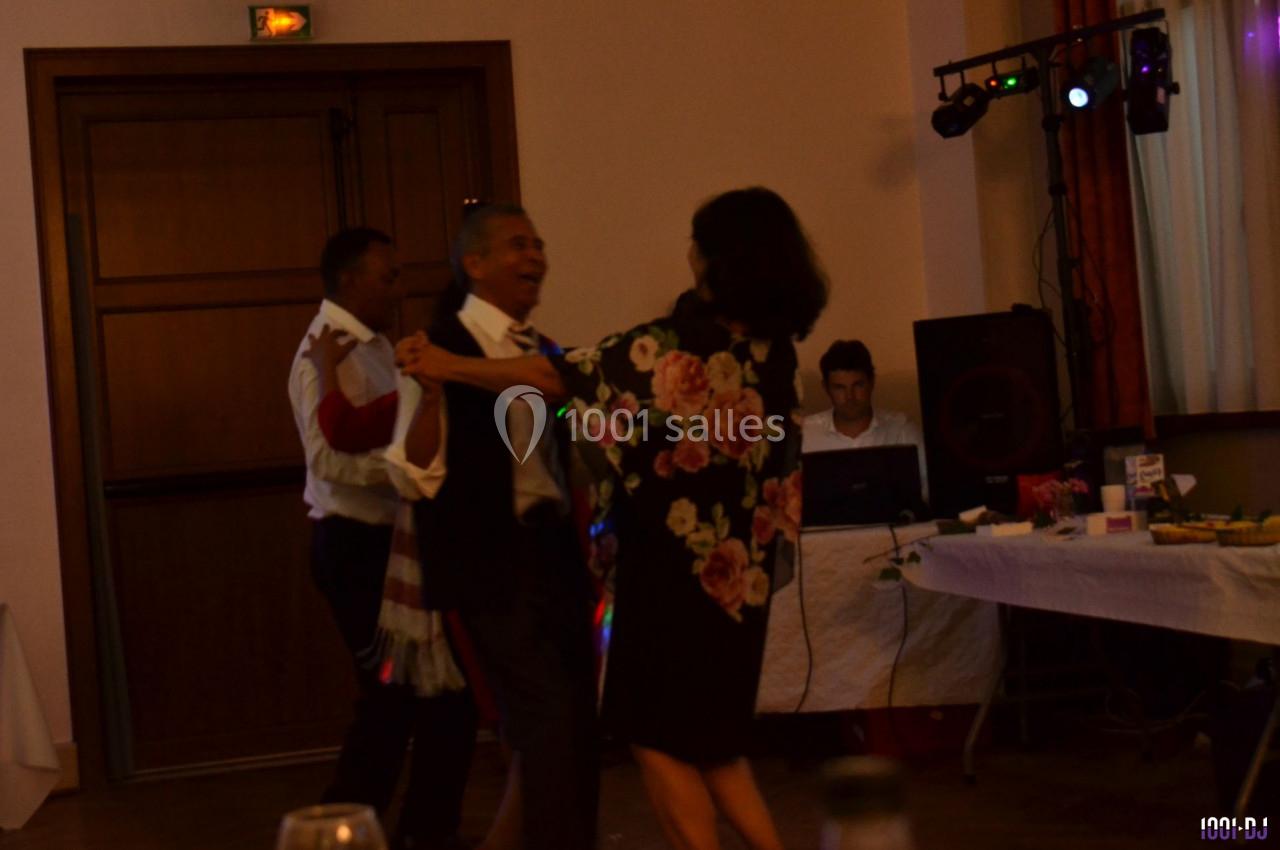 Des personnes dansent dans une salle éclairée, avec un DJ en arrière-plan et une table dressée sur le côté.