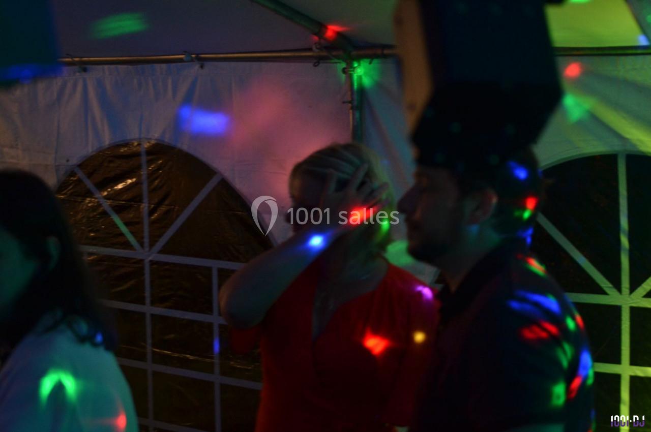 Personnes dansant sous des lumières colorées dans une ambiance festive, avec une tente visible en arrière-plan.
