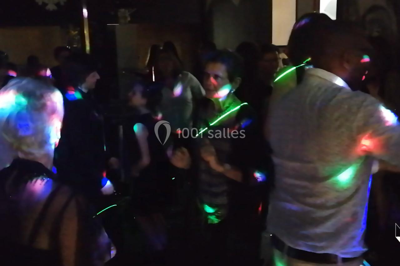 Des personnes dansent dans une ambiance festive avec des lumières colorées dans une salle sombre.