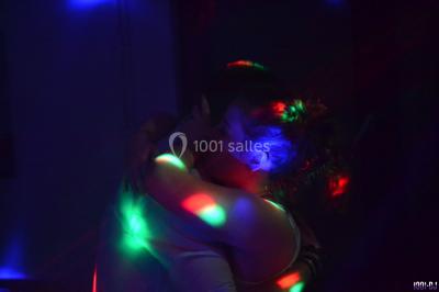 Salle polyvalente avec scène surélevée, rideaux bleus, écran blanc, tables et chaises disposées en avant-plan.