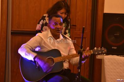 Salle polyvalente avec scène surélevée, rideaux bleus, écran blanc, tables et chaises disposées en avant-plan.