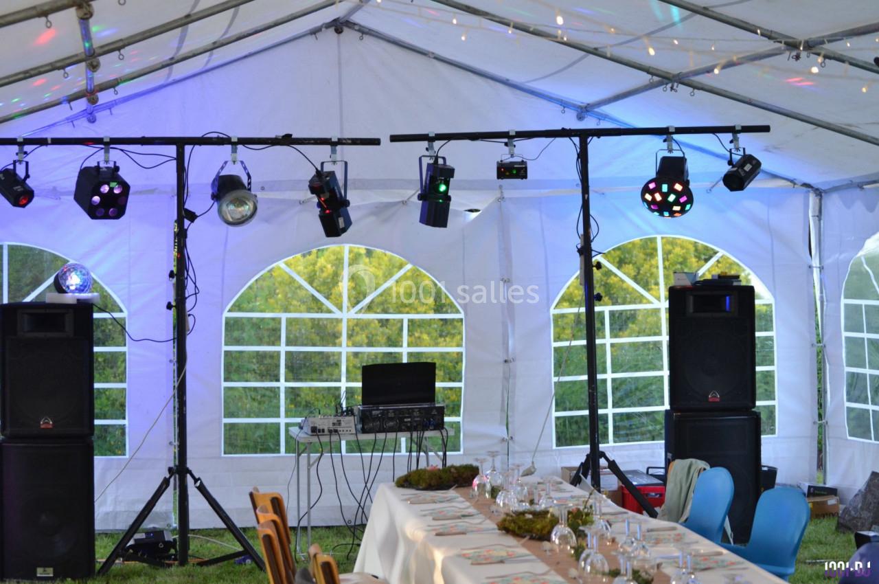 Installation de matériel d'éclairage et de sonorisation sous une tente blanche, avec tables dressées pour un événement.