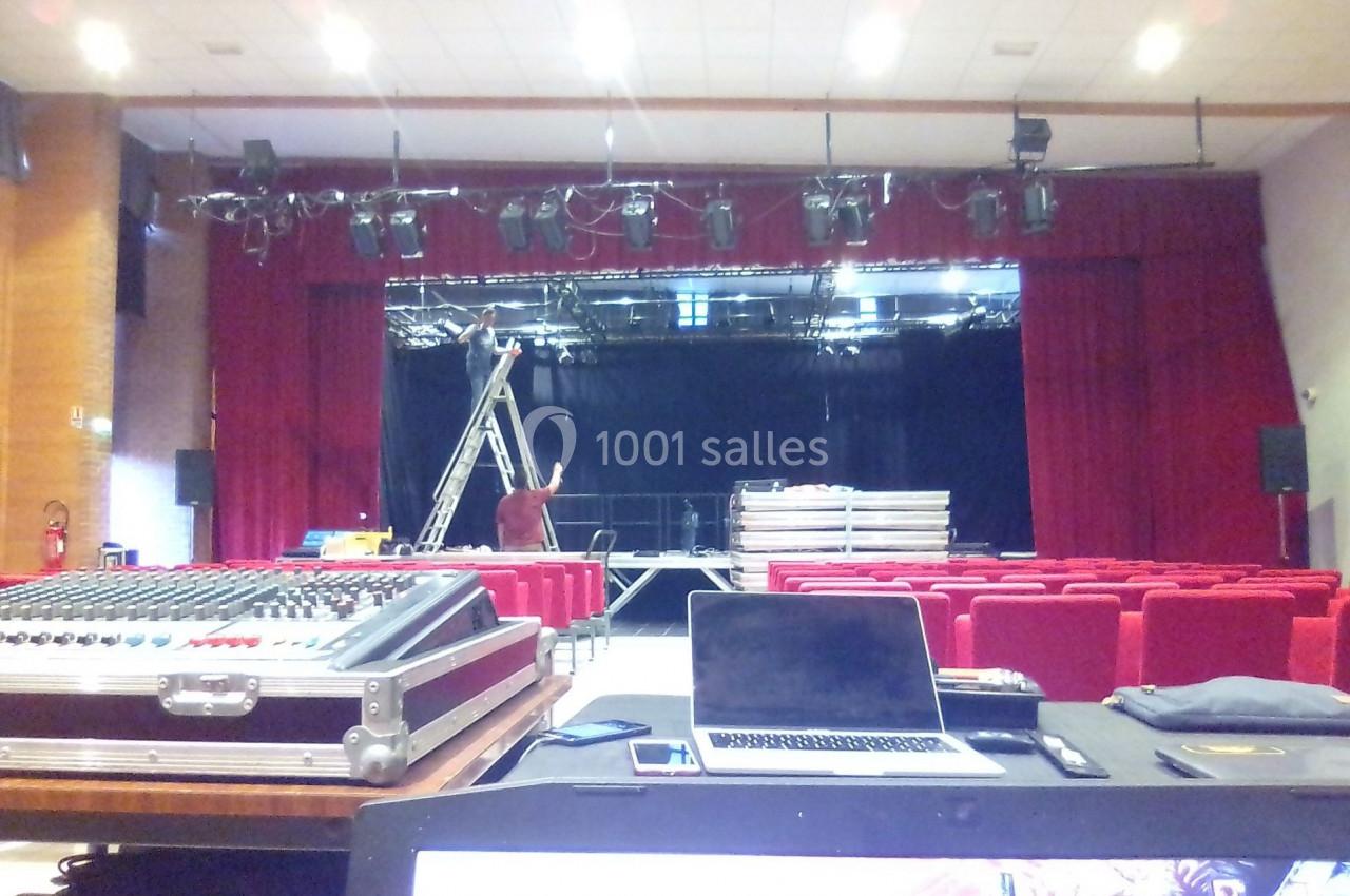Salle de spectacle en préparation avec un technicien sur une échelle et des équipements audiovisuels au premier plan.