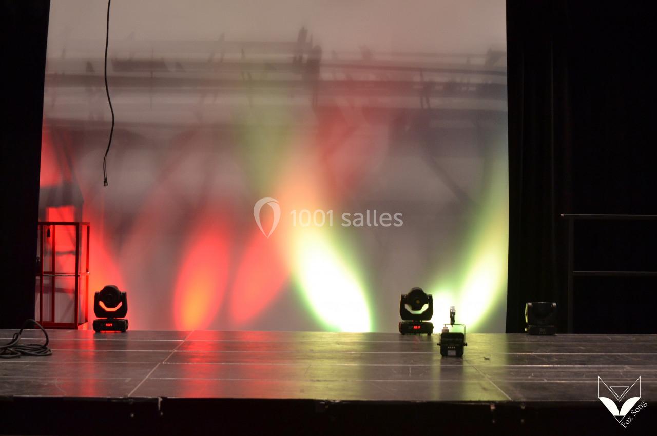 Scène vide avec éclairage coloré rouge et vert, câbles visibles et arrière-plan flou.