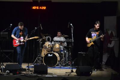 Salle polyvalente avec scène surélevée, rideaux bleus, écran blanc, tables et chaises disposées en avant-plan.