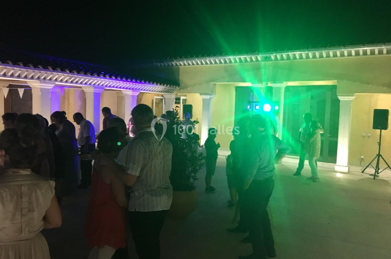 Groupe de personnes dansant et discutant lors d'une soirée en extérieur, éclairée par des lumières colorées.