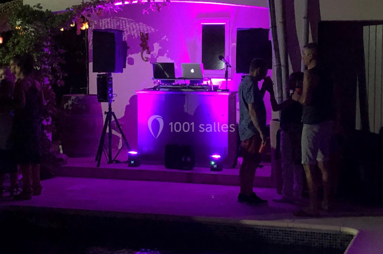 Scène de soirée en extérieur avec éclairage violet, une table de mixage et des personnes discutant près d'une piscine.