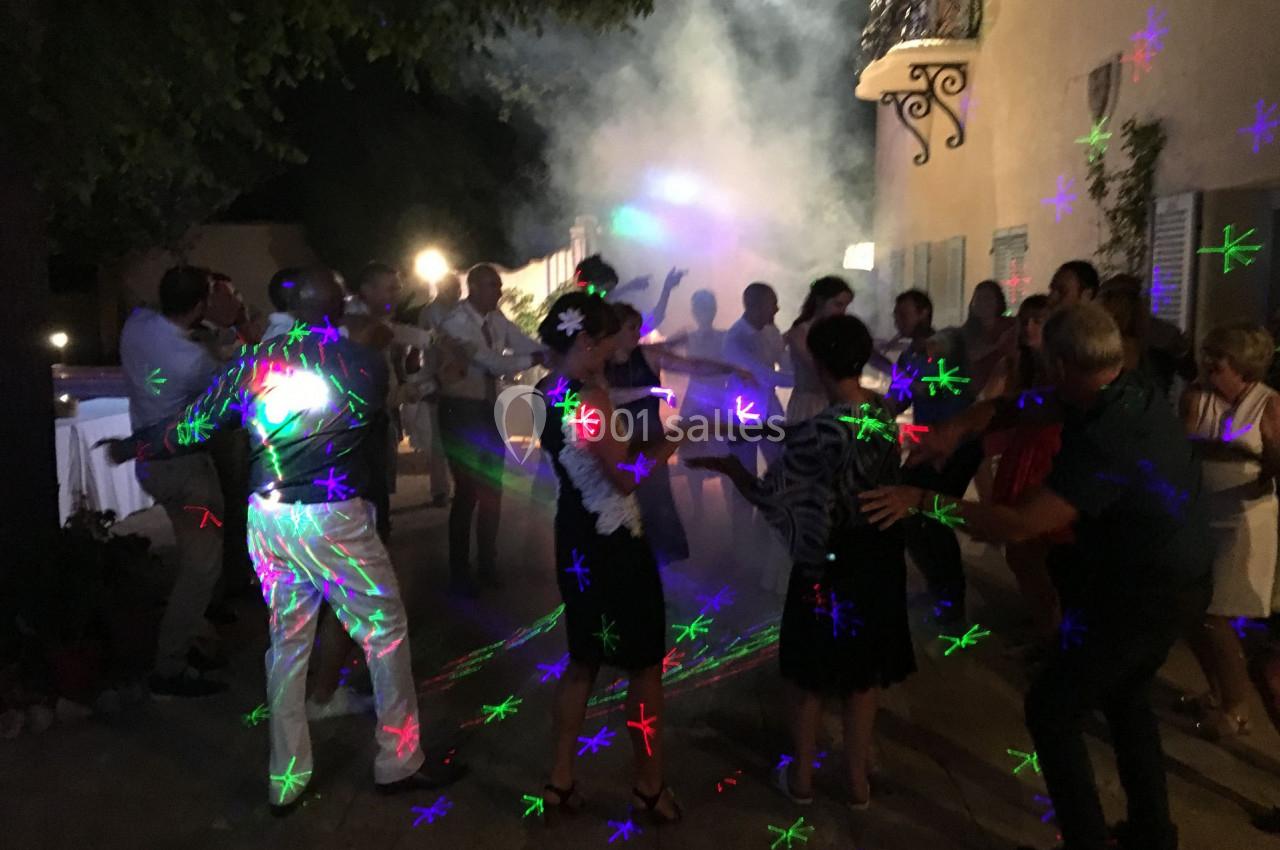 Groupe de personnes dansant en soirée en extérieur, éclairées par des lumières colorées et entourées de fumée.