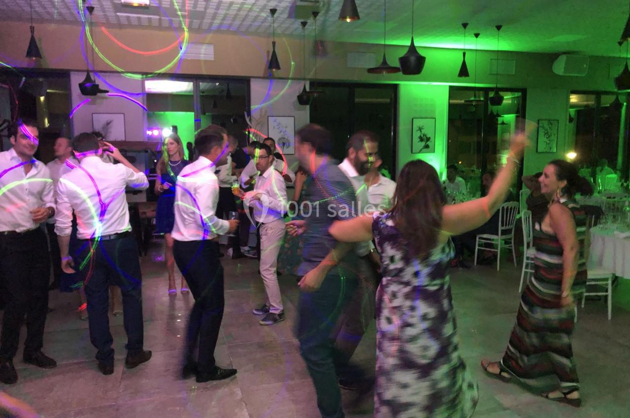 Des personnes dansent dans une salle éclairée par des lumières colorées, avec des tables dressées en arrière-plan.