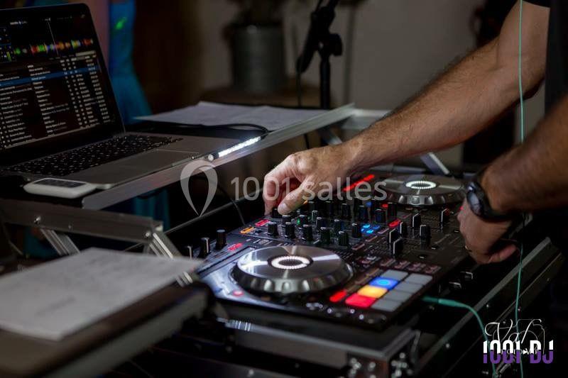 Un DJ utilise une table de mixage avec un ordinateur portable à proximité dans un environnement intérieur.