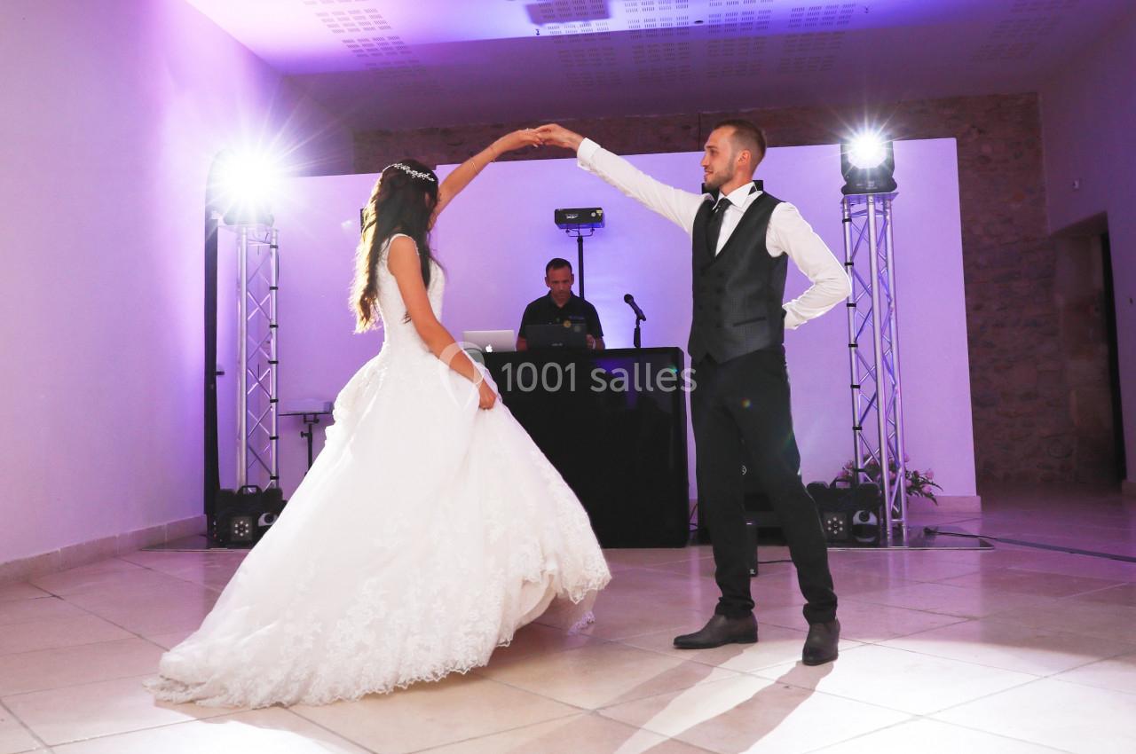 Un couple danse lors d'une réception, la mariée en robe blanche et le marié en costume, sous des lumières de scène.