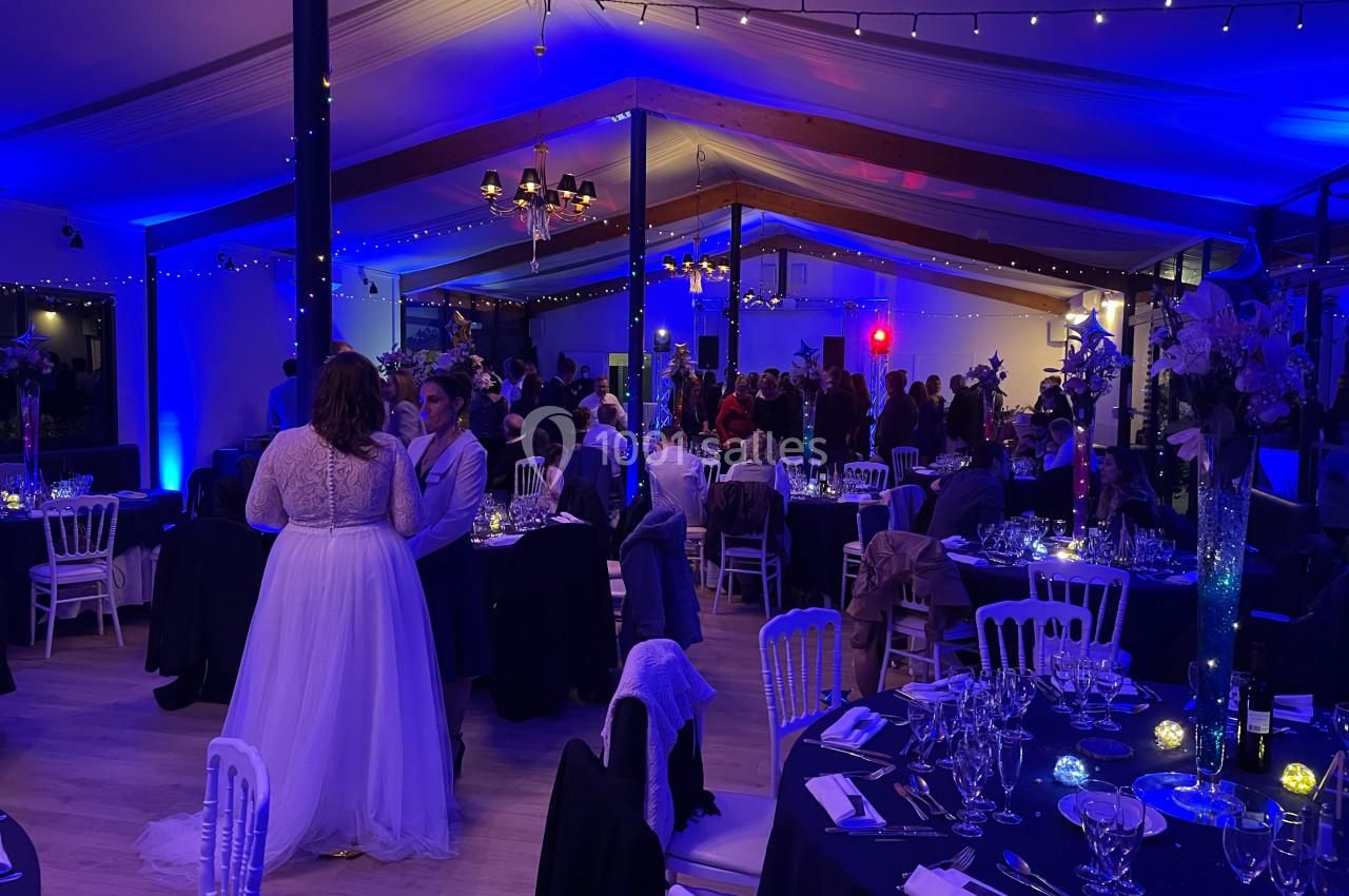 Salle de réception décorée avec des lumières bleues, des tables dressées et des invités en tenue de soirée.