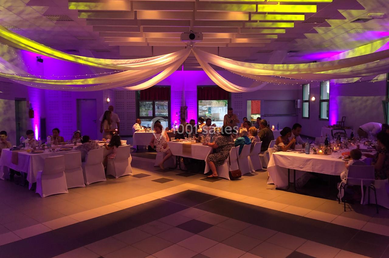 Salle décorée avec des drapés et éclairages colorés, accueillant des convives assis à des tables lors d'un événement.