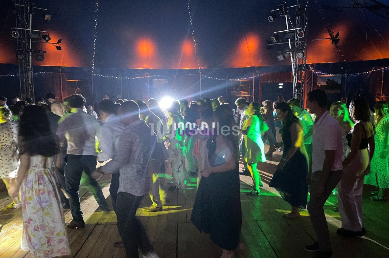 Personnes dansant sous une tente éclairée par des lumières colorées, ambiance festive et conviviale.