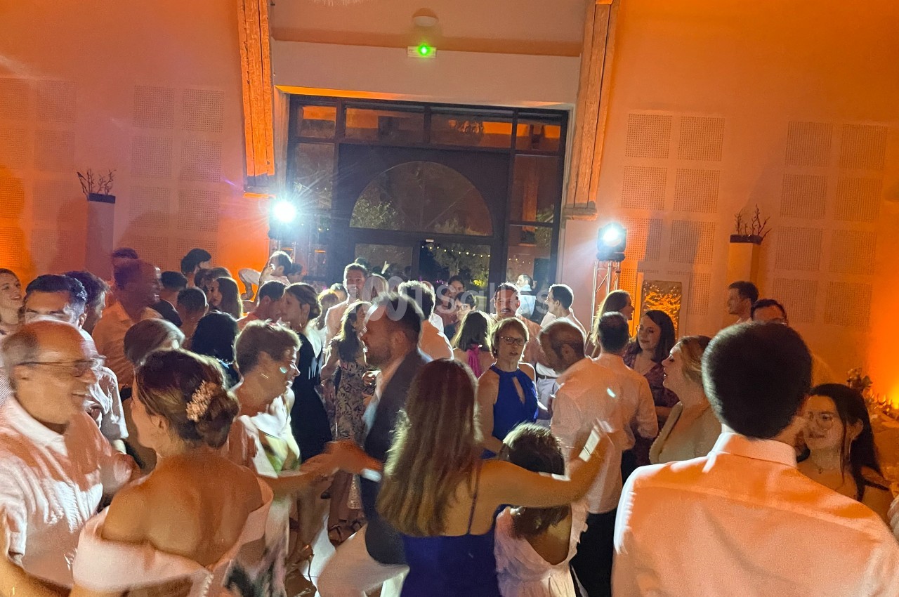 Des personnes dansent lors d'une fête dans une salle éclairée par des lumières chaudes et des projecteurs.