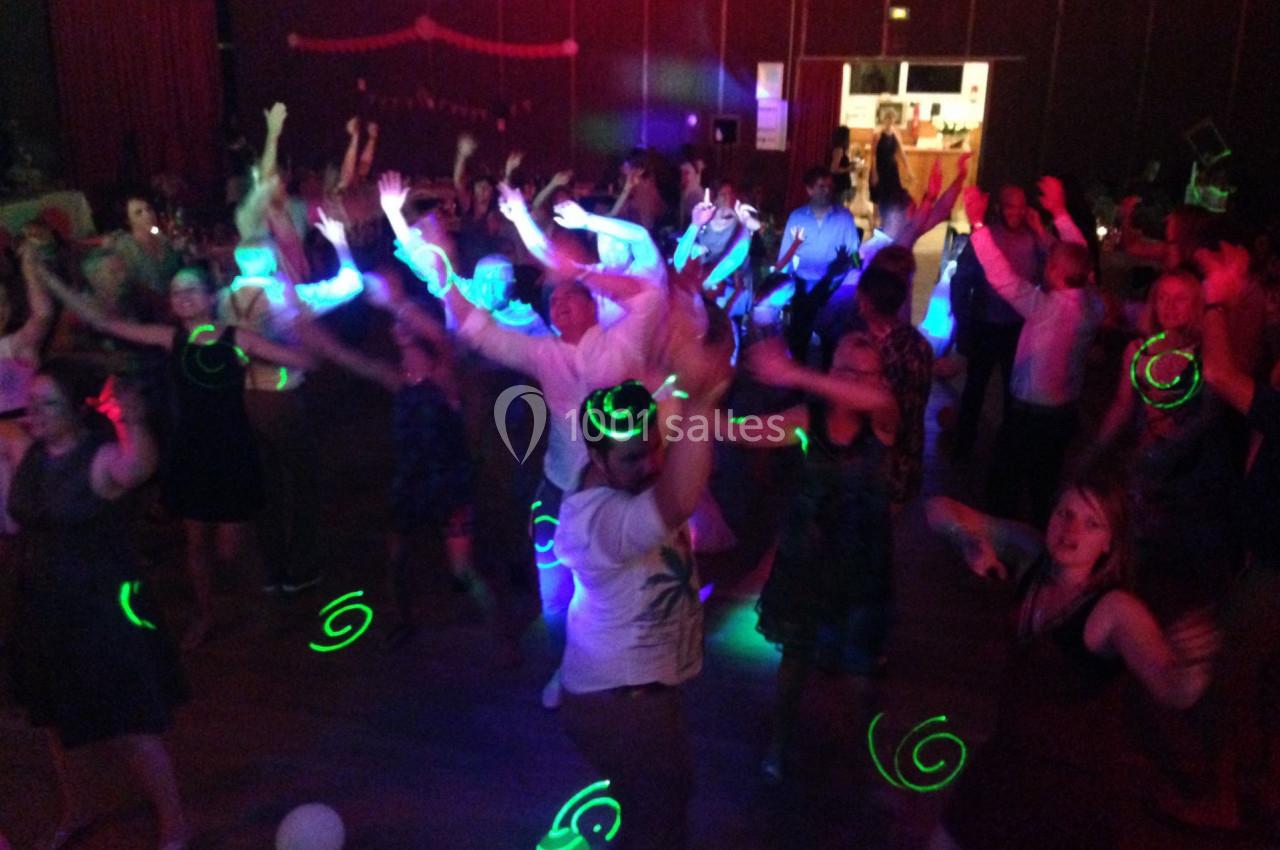 Des personnes dansent dans une salle sombre avec des lumières colorées et des effets lumineux verts.