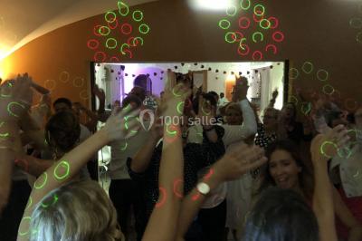 Salle de réception avec des invités assis à des tables, éclairée par des guirlandes lumineuses suspendues.