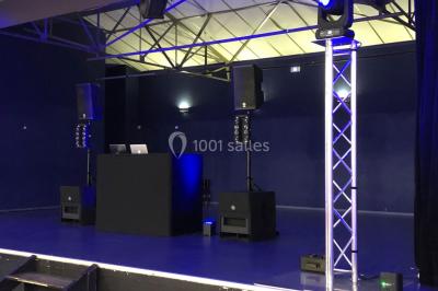 Salle de réception avec des invités assis à des tables, éclairée par des guirlandes lumineuses suspendues.