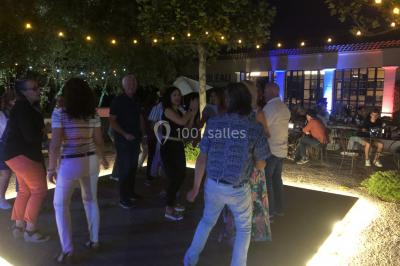 Salle de réception avec des invités assis à des tables, éclairée par des guirlandes lumineuses suspendues.