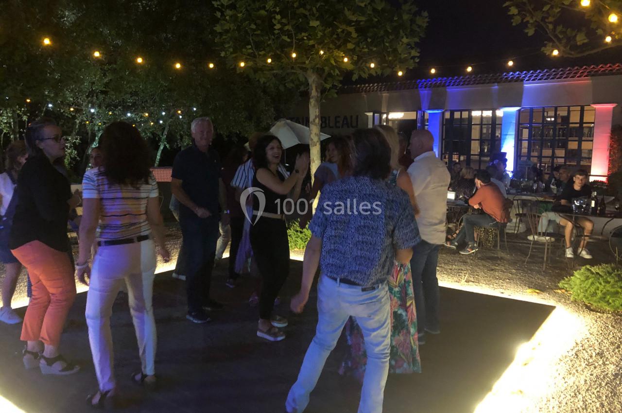 Des personnes dansent en extérieur le soir, sous des guirlandes lumineuses, près d'un bâtiment éclairé.