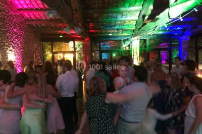 Salle de réception avec des invités assis à des tables, éclairée par des guirlandes lumineuses suspendues.