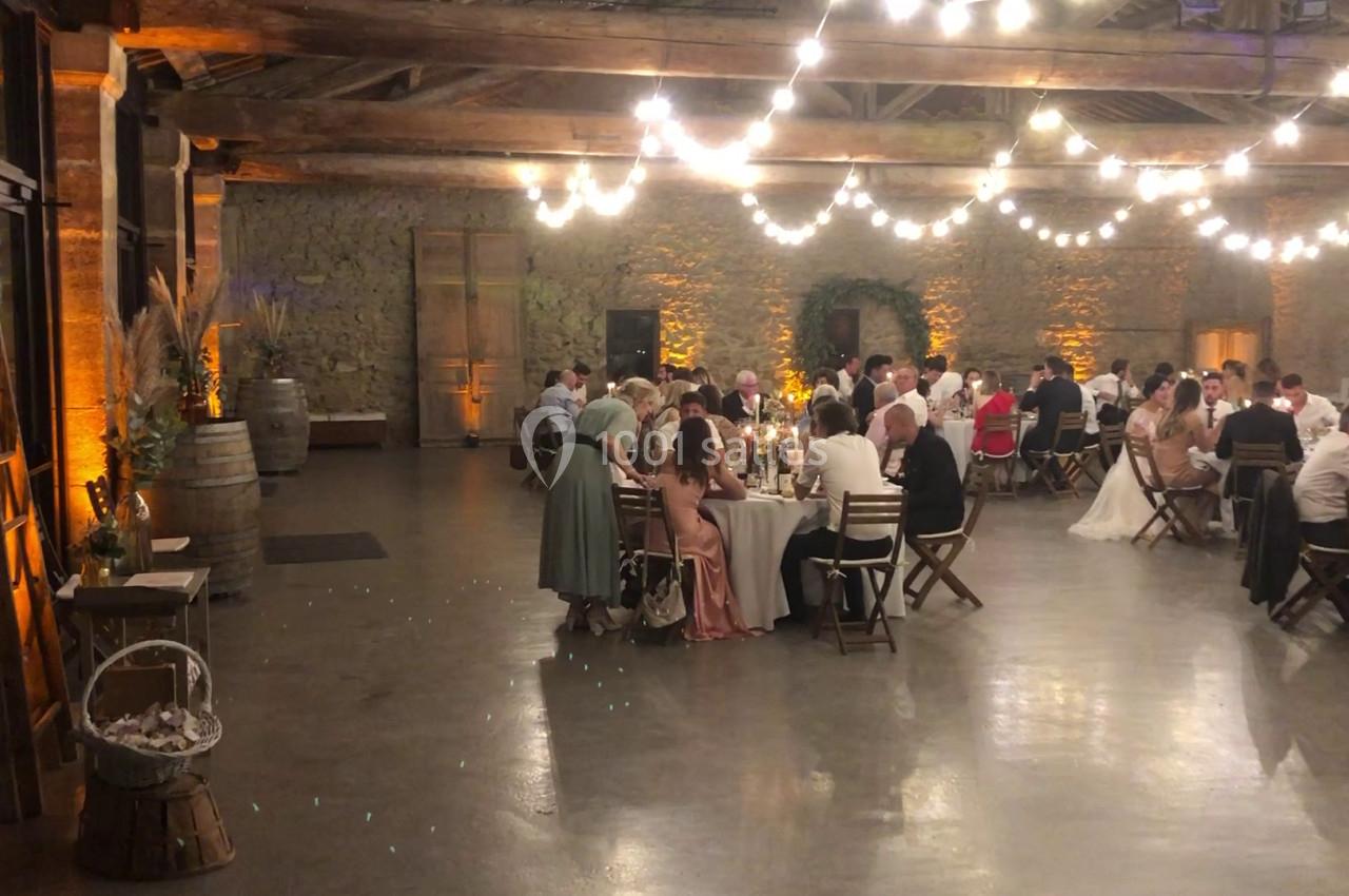 Salle de réception avec des invités assis à des tables, éclairée par des guirlandes lumineuses suspendues.