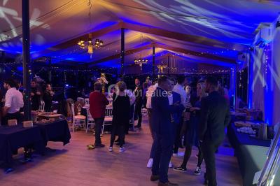 Salle de réception avec des invités assis à des tables, éclairée par des guirlandes lumineuses suspendues.