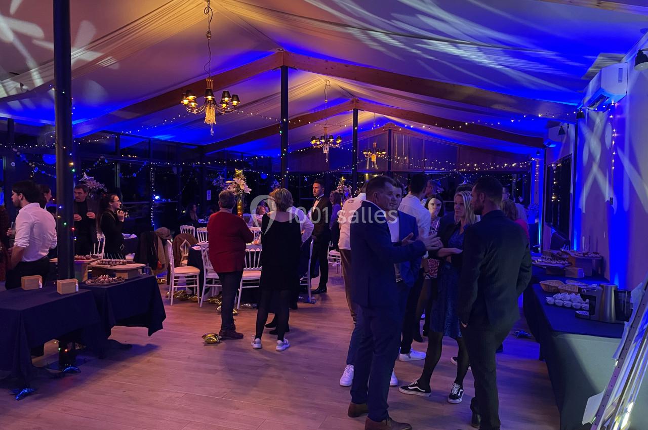 Personnes discutant dans une salle éclairée par des lumières bleues, avec tables et décorations festives.