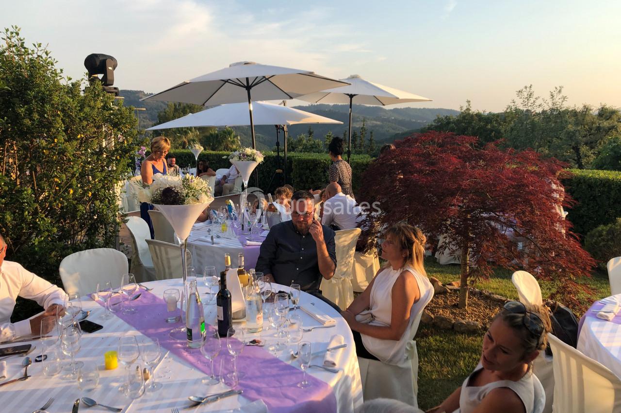 Des convives assis à des tables décorées en extérieur, sous des parasols, avec un paysage vallonné en arrière-plan.