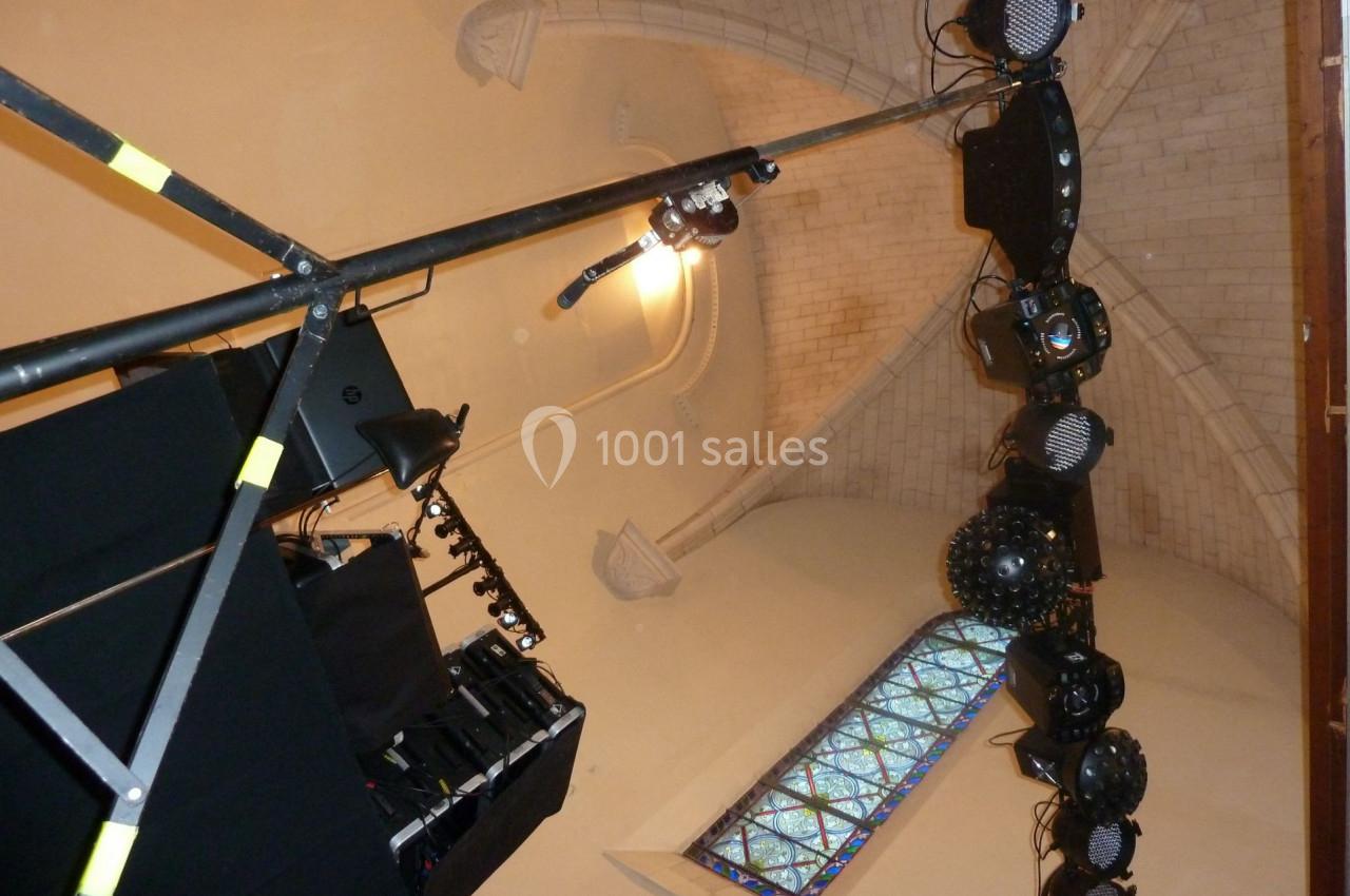 Installation d'éclairage scénique suspendue dans un bâtiment avec plafond voûté et vitrail en arrière-plan.