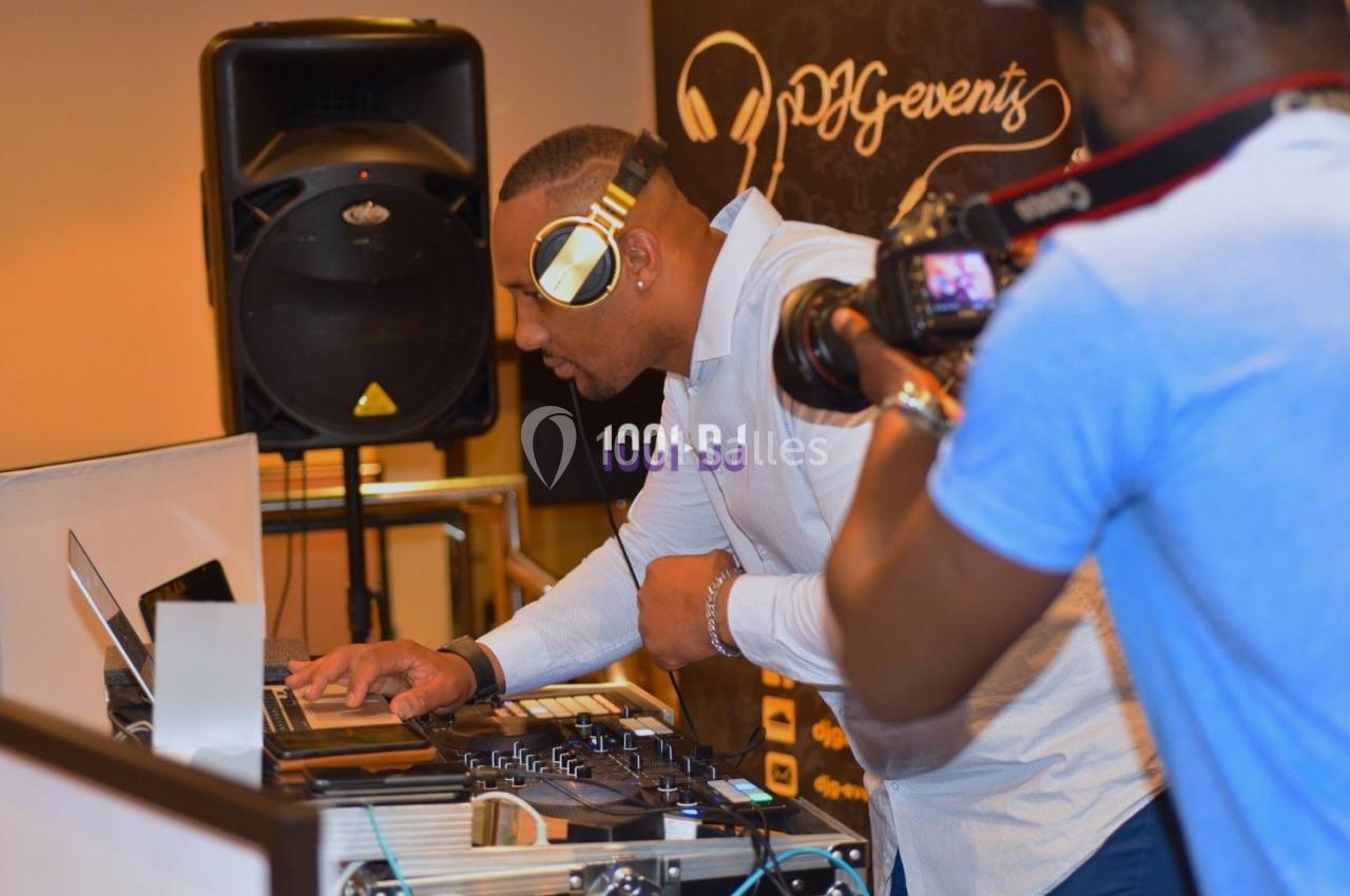 Un DJ mixe sur une table de mixage, avec un photographe en train de le filmer au premier plan.