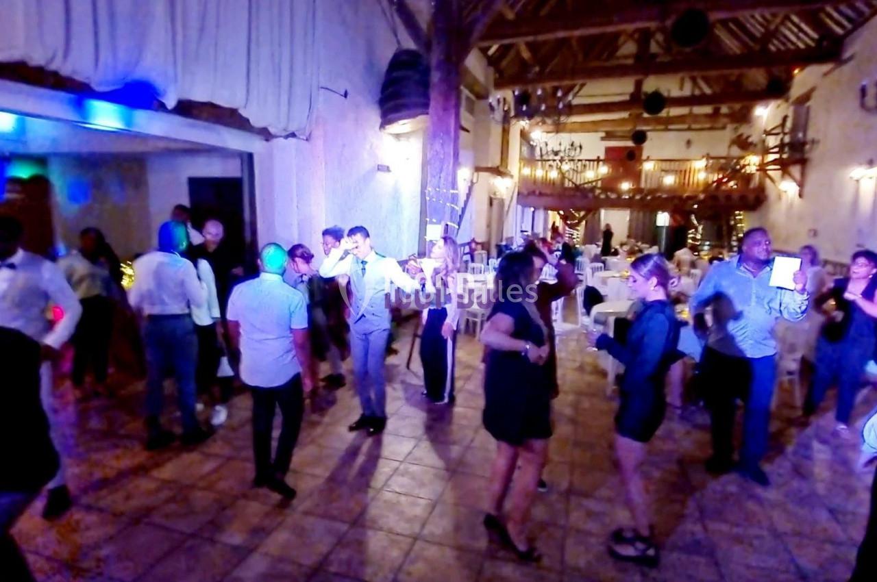 Des personnes dansent et discutent dans une salle de réception éclairée, avec des tables décorées en arrière-plan.