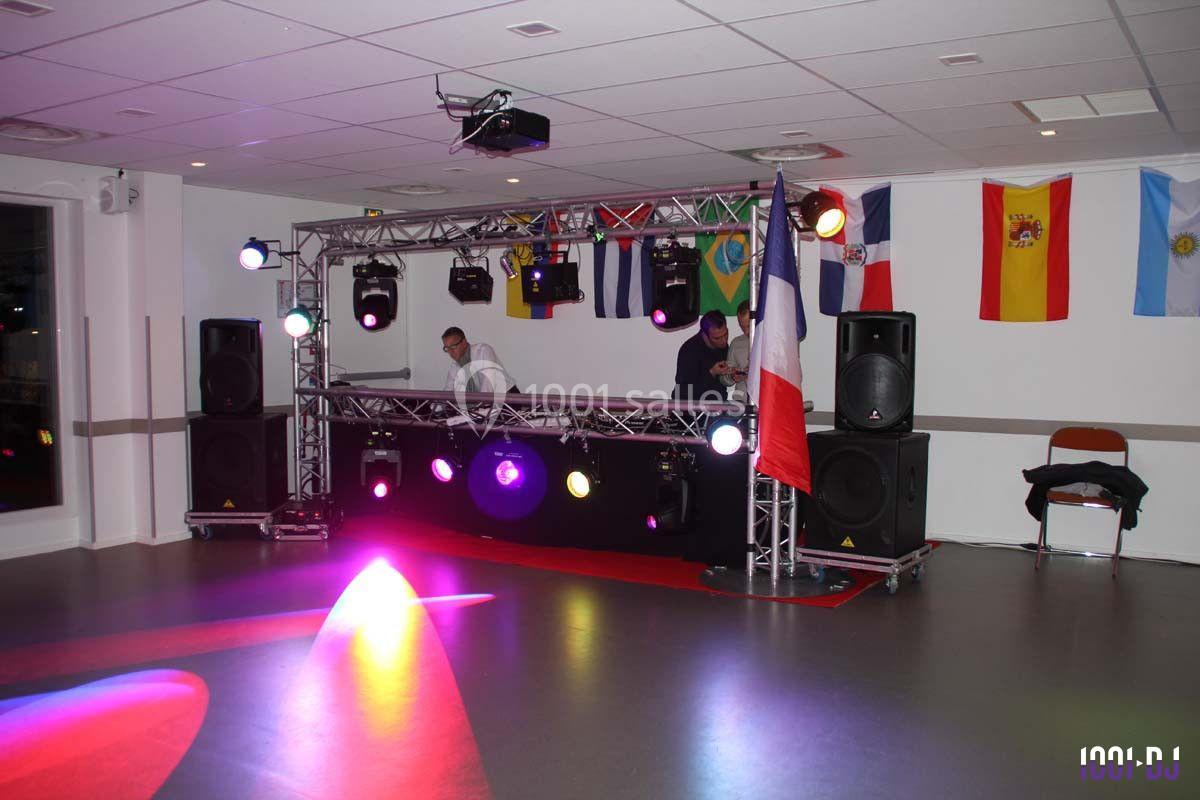 Deux DJ mixent sur une scène éclairée avec des drapeaux internationaux en arrière-plan dans une salle de réception.