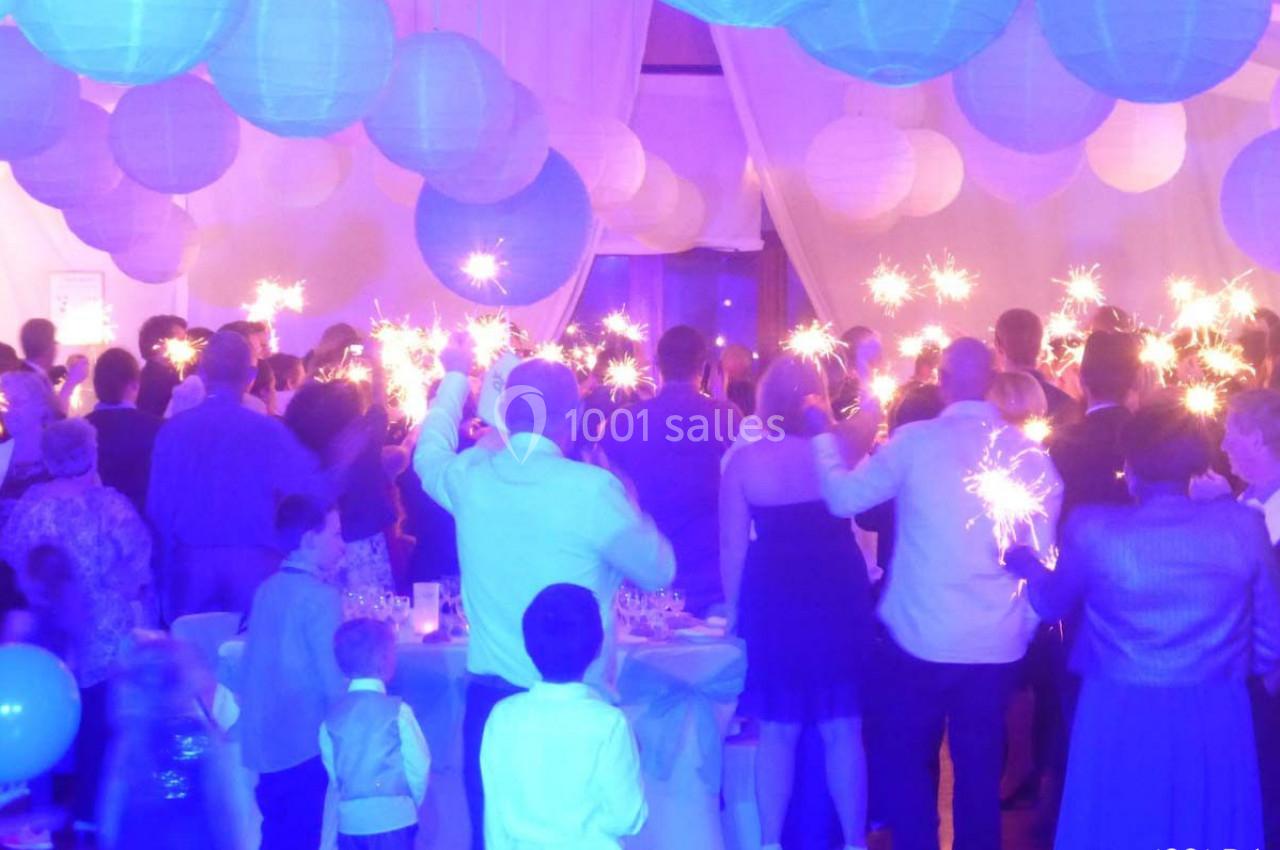 Groupe de personnes tenant des cierges magiques dans une salle décorée de lanternes suspendues et éclairée en bleu.