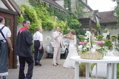 Salle de réception décorée avec des tables dressées, nappes blanches, chaises houssées et arrangements floraux.