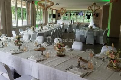 Salle de réception décorée avec des tables dressées, nappes blanches, chaises houssées et arrangements floraux.