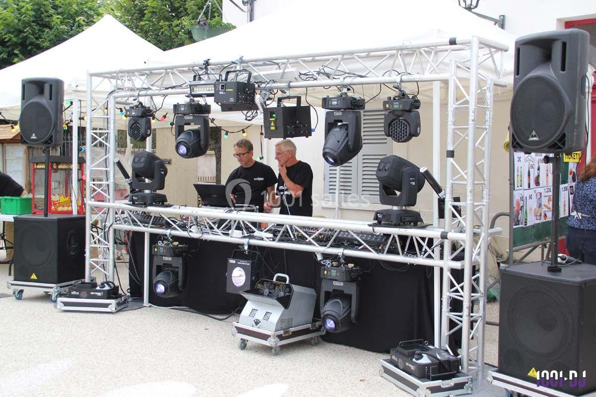 Deux personnes gèrent une installation de matériel d'éclairage et de sonorisation sur une scène extérieure.