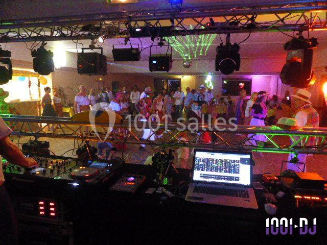 Vue d'une soirée dansante avec une table de mixage au premier plan et des invités sur la piste éclairée.