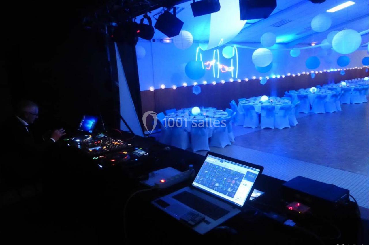 Salle de réception décorée de lumières bleues avec une table de mixage et un DJ en arrière-plan.