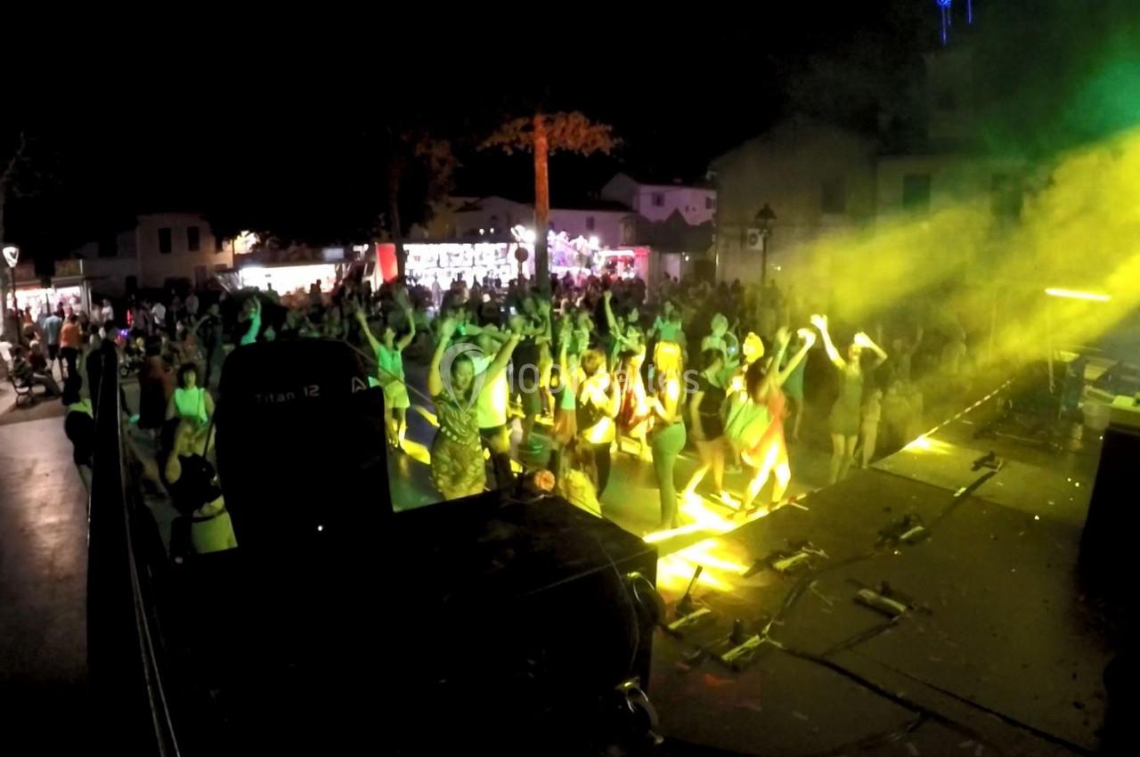 Foule dansant devant une scène éclairée par des projecteurs jaunes lors d'un concert en plein air de nuit.