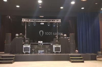 Salle avec éclairage de scène coloré, piste de danse illuminée, tables sur les côtés et matériel audio en arrière-plan.