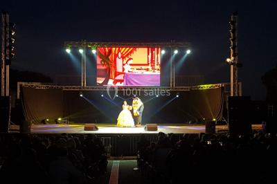 Salle avec éclairage de scène coloré, piste de danse illuminée, tables sur les côtés et matériel audio en arrière-plan.