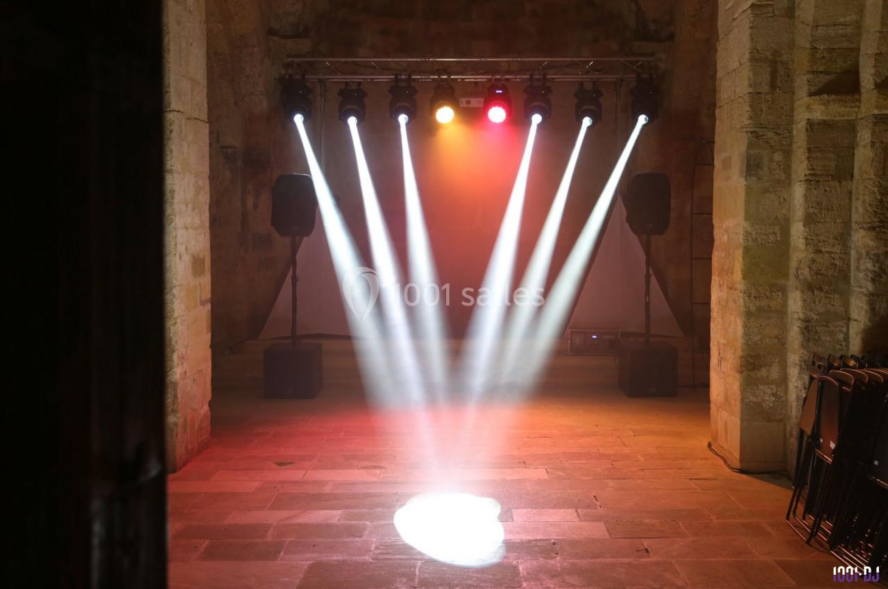 Projecteurs lumineux éclairant une scène vide dans une salle en pierre avec des murs anciens et des enceintes.