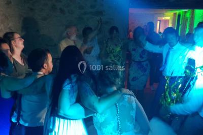 Salle avec éclairage de scène coloré, piste de danse illuminée, tables sur les côtés et matériel audio en arrière-plan.