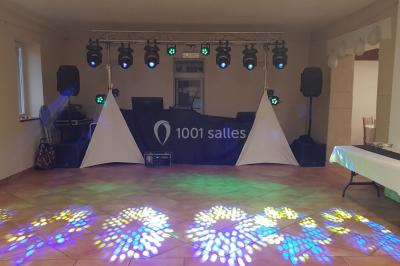 Salle avec éclairage de scène coloré, piste de danse illuminée, tables sur les côtés et matériel audio en arrière-plan.